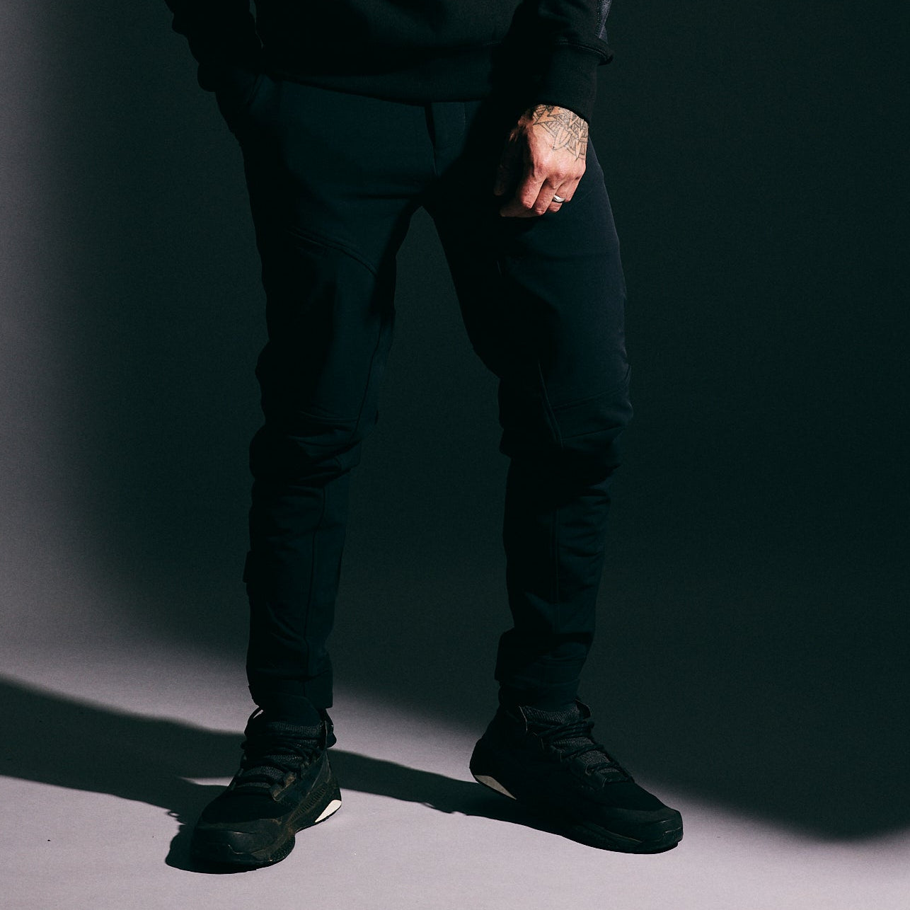 Man wearing a black hoodie and pants against a dark background